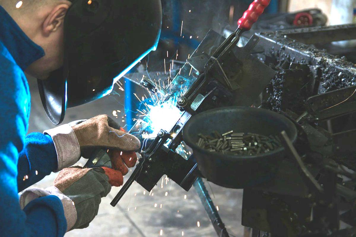 A welder working on a steel assembly, generating the fume and noise that make respiratory and hearing surveillance a legal duty